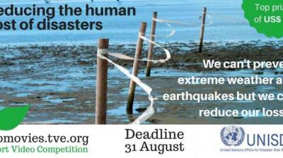 Banner promoting a video competition on reducing disaster costs, featuring warning tape on wooden posts, competition deadline, and UNISDR logo.