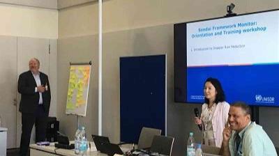 People conducting a training workshop with a presentation on a screen, a flip chart with notes, and two people standing while one is seated and smiling.