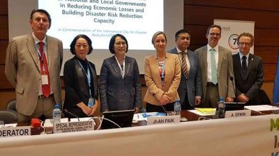 A group of seven professionals stand in front of a presentation screen at a conference on disaster risk reduction.