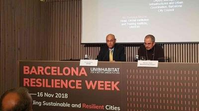 Two men seated at a conference table during Barcelona Resilience Week 2018, with a presentation projected behind them.