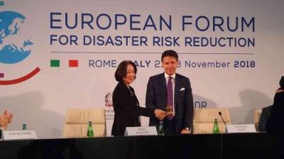 Two people stand and shake hands on stage at the European Forum for Disaster Risk Reduction in Rome, Italy, November 2018. Event signage is visible in the background.