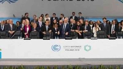 A large group of people in formal attire stands on a stage behind a table at the COP24 climate conference in Poland, 2018.