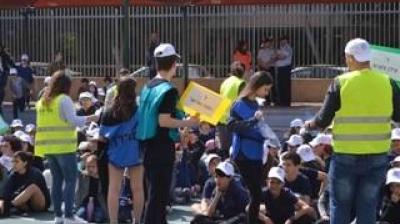 A group of people wearing safety vests and caps gather outdoors near a fence, facing a seated crowd.