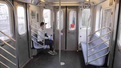 A person wearing a mask and gloves sits alone on a mostly empty subway train.