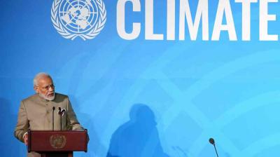 A man speaks at a podium in front of a blue backdrop displaying the United Nations emblem and the word "CLIMATE.