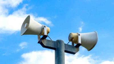 Dos altavoces montados en un poste contra un cielo azul con nubes blancas.