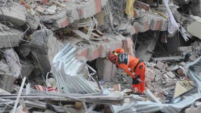 Rescue worker in orange gear searches through debris of a collapsed building.