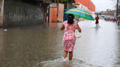 A woman holding an umbrella walks through a flooded street during heavy rain, with other people visible in the background.