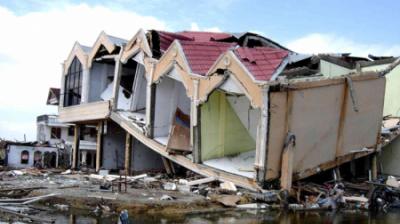 A partially collapsed building with debris scattered around, reflecting severe structural damage.