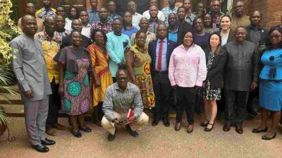 A large group of people, both men and women, stand and pose for a group photo on steps outside a brick building.
