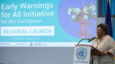 Person speaking at a podium with the United Nations logo, in front of a screen displaying "Early Warnings for All Initiative for the Caribbean: Regional Launch.
