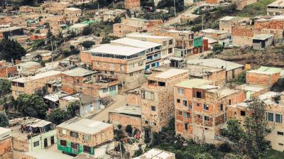 Cluster of densely packed, unfinished brick and concrete houses on a hillside, some with metal roofs and visible signs of wear.