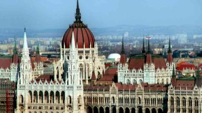 Hungarian Parliament Building with its central dome and spires, set against a cityscape background under a clear sky.