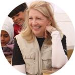 A woman wearing a beige vest and smiling, seated next to two children.