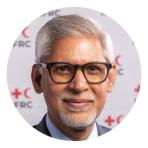 A man with gray hair and glasses is smiling in front of a backdrop featuring red crosses and the acronym "FRC.