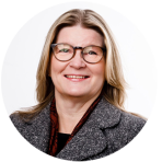 A woman with shoulder-length blonde hair, wearing glasses, a gray blazer, and a maroon scarf, smiling at the camera against a plain white background.